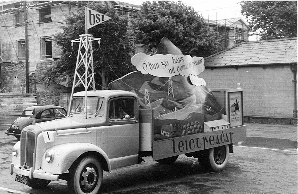 Black-and-white photograph of an ESB promotional vehicle decorated with a display about rural electrification and electricity infrastructure.